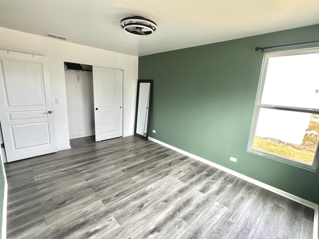 unfurnished bedroom with visible vents, multiple windows, baseboards, and wood finished floors