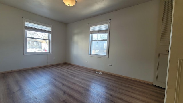 spare room featuring visible vents, plenty of natural light, baseboards, and wood finished floors