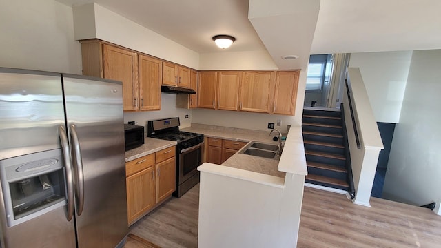 kitchen with a peninsula, light wood-style flooring, a sink, stainless steel appliances, and under cabinet range hood