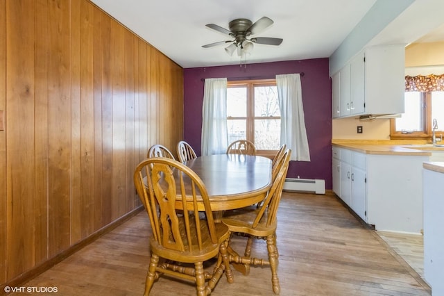 dining space with a baseboard heating unit, wooden walls, light wood-style flooring, and a ceiling fan