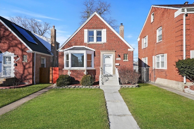 view of front of house featuring brick siding, a chimney, a front lawn, and fence