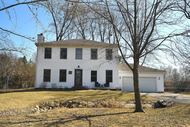 colonial-style house featuring aphalt driveway, a trampoline, a front yard, a garage, and a chimney