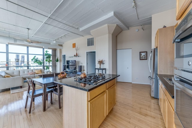 kitchen featuring light brown cabinetry, stainless steel appliances, open floor plan, rail lighting, and light wood-type flooring