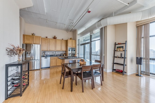 dining space featuring light wood-type flooring, baseboards, a towering ceiling, and rail lighting