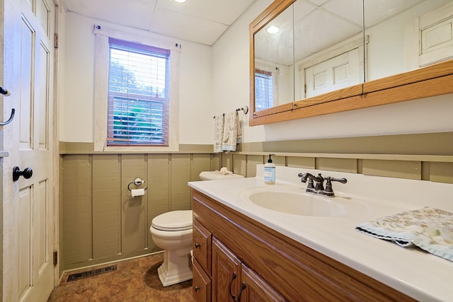 half bathroom featuring visible vents, toilet, vanity, and a wainscoted wall