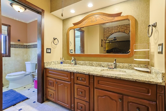 bathroom with tile walls, toilet, double vanity, and a sink