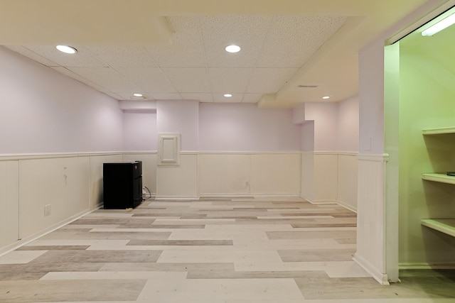 finished basement with a wainscoted wall, recessed lighting, freestanding refrigerator, and wood finished floors