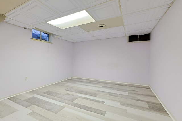 finished below grade area with a drop ceiling, baseboards, visible vents, and light wood-style flooring