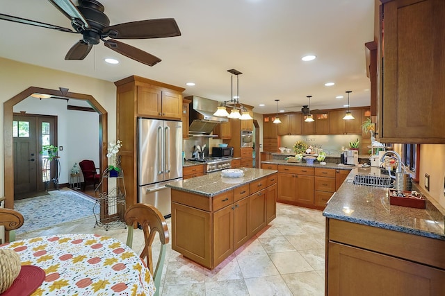 kitchen with a ceiling fan, dark stone countertops, arched walkways, appliances with stainless steel finishes, and wall chimney exhaust hood