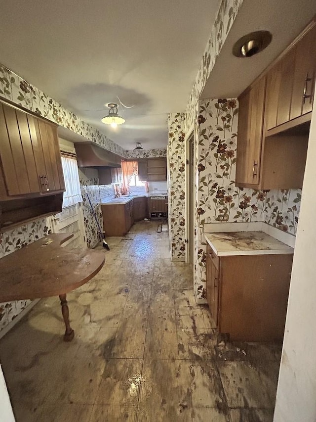 kitchen featuring brown cabinets, a ceiling fan, wallpapered walls, hardwood / wood-style floors, and light countertops