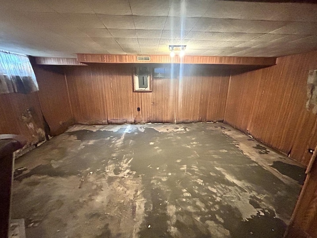 unfinished basement with wooden walls, visible vents, and a drop ceiling