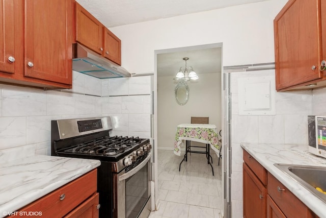 kitchen with under cabinet range hood, gas range, brown cabinets, an inviting chandelier, and marble finish floor