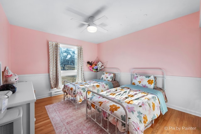 bedroom featuring baseboard heating, wood finished floors, and a ceiling fan