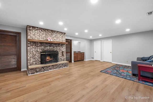 living area featuring visible vents, baseboards, recessed lighting, light wood-style floors, and a brick fireplace