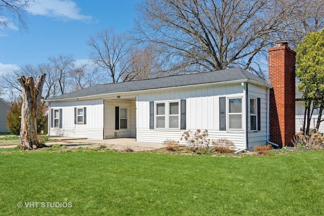 view of front of house with a chimney, board and batten siding, a front lawn, and a patio area