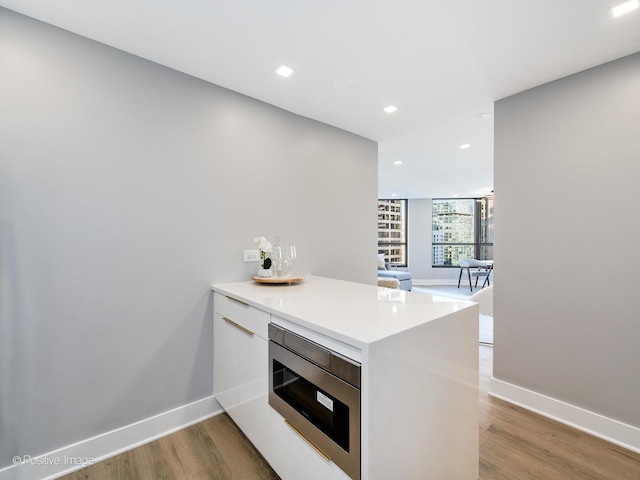 kitchen with stainless steel microwave, light wood-style flooring, a peninsula, white cabinets, and modern cabinets