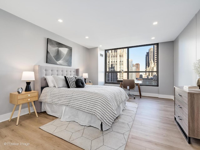 bedroom featuring recessed lighting, baseboards, light wood-style floors, and a city view