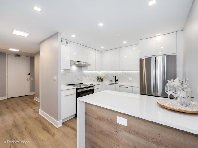 kitchen with under cabinet range hood, white cabinets, stainless steel appliances, modern cabinets, and a sink