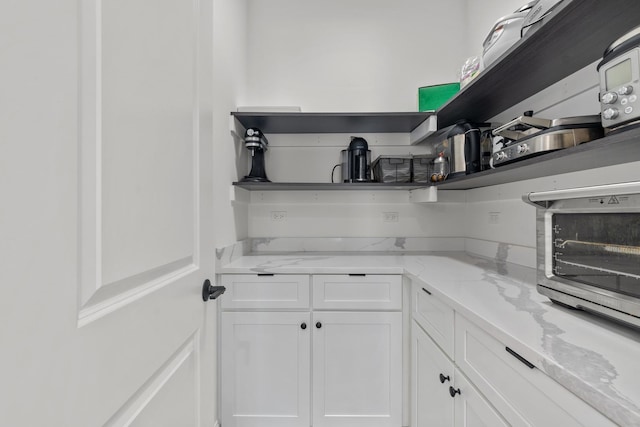 kitchen featuring open shelves, light stone countertops, and white cabinetry