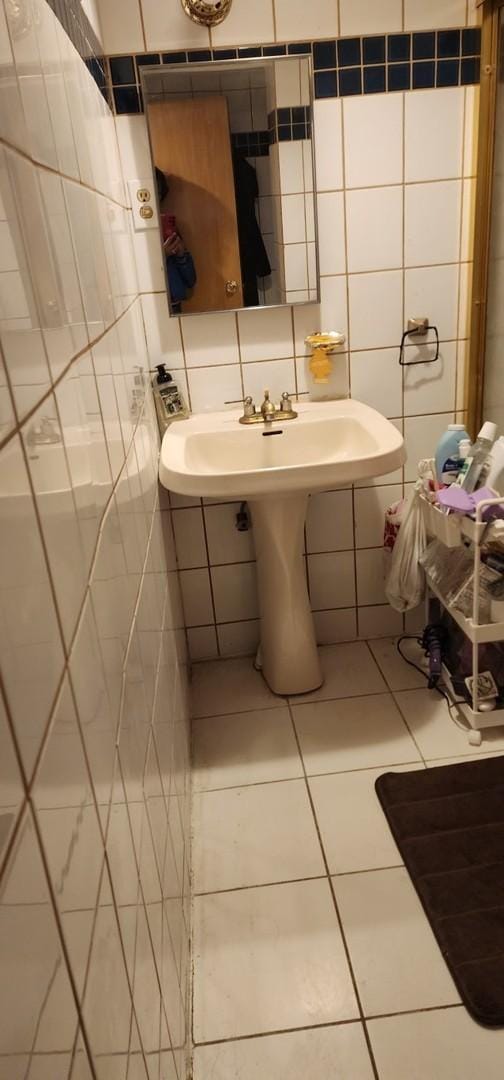 half bathroom with tile patterned flooring, backsplash, tile walls, and a sink