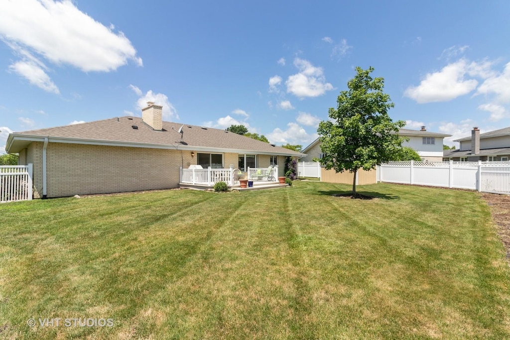 rear view of property featuring brick siding, a fenced backyard, a lawn, and a chimney