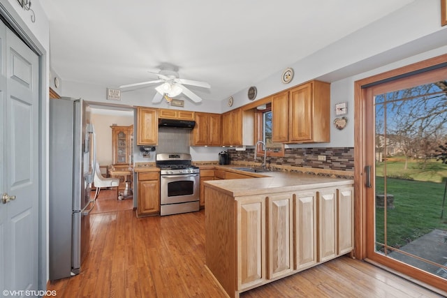 kitchen featuring a peninsula, a sink, under cabinet range hood, appliances with stainless steel finishes, and light wood-type flooring