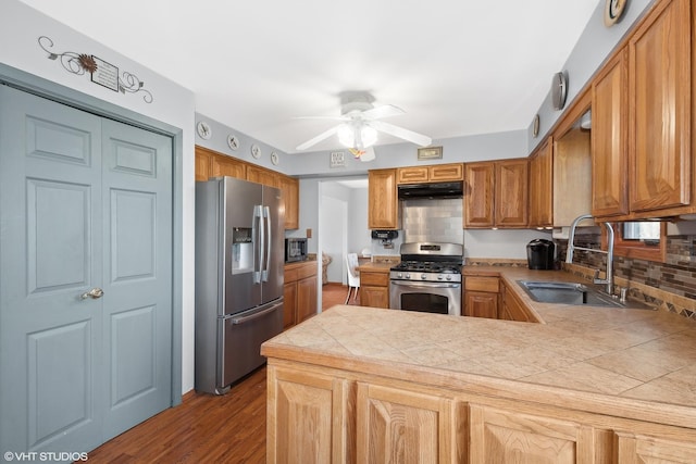 kitchen with a ceiling fan, a sink, under cabinet range hood, stainless steel appliances, and a peninsula