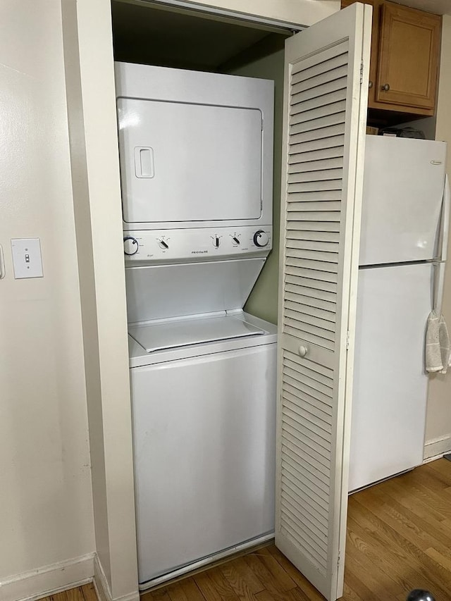 clothes washing area with laundry area, stacked washer / dryer, wood finished floors, and baseboards