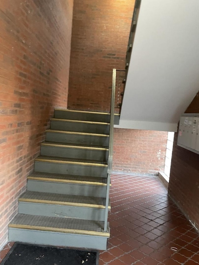 stairway featuring brick floor and brick wall