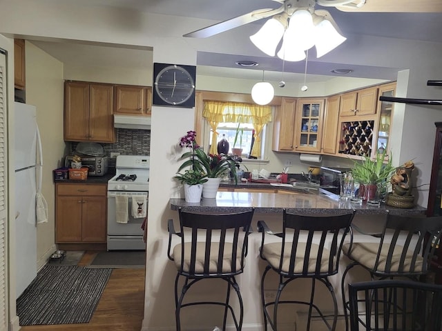 kitchen featuring under cabinet range hood, white appliances, a peninsula, glass insert cabinets, and ceiling fan