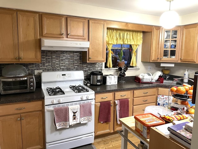 kitchen featuring glass insert cabinets, under cabinet range hood, a toaster, white range with gas stovetop, and light wood-style floors