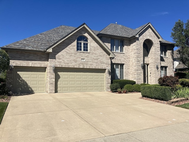 french country inspired facade featuring concrete driveway, a garage, and brick siding