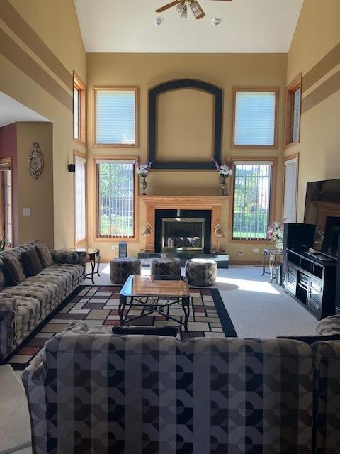 living area with a glass covered fireplace, high vaulted ceiling, ceiling fan, and carpet flooring