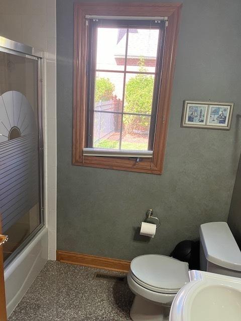 full bathroom with visible vents, baseboards, bath / shower combo with glass door, toilet, and a sink