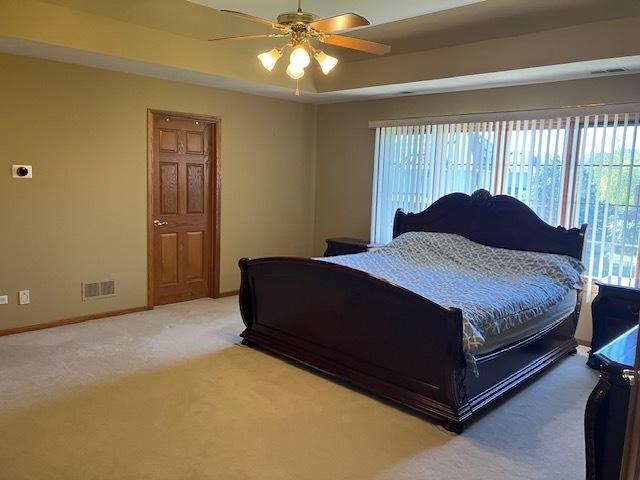 bedroom with visible vents, a tray ceiling, baseboards, light colored carpet, and ceiling fan