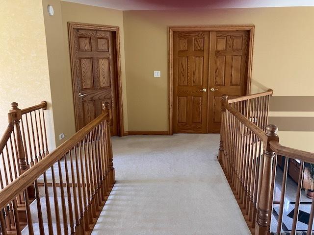 hall with an upstairs landing, baseboards, and light carpet