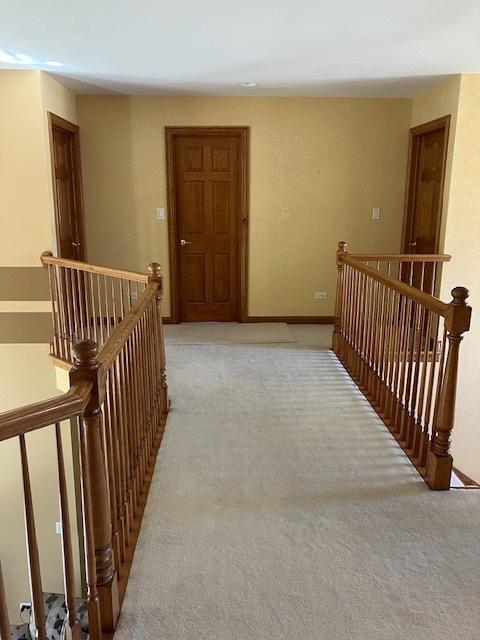 corridor with an upstairs landing and light carpet