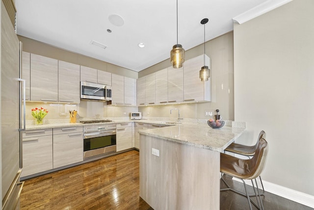 kitchen featuring dark wood-type flooring, light stone counters, a kitchen breakfast bar, appliances with stainless steel finishes, and a peninsula