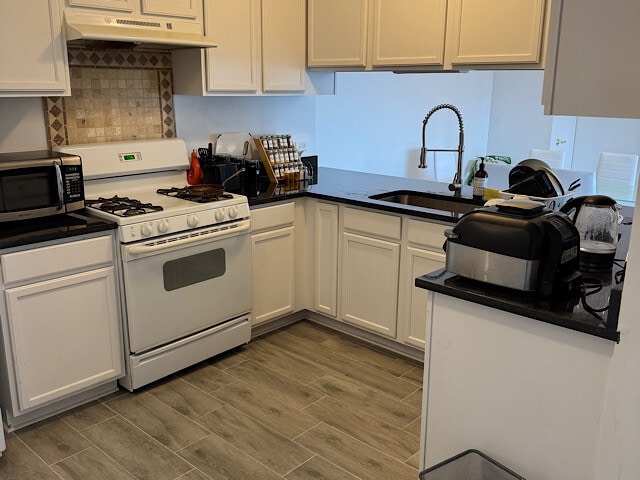 kitchen with wood tiled floor, white range with gas cooktop, a sink, under cabinet range hood, and stainless steel microwave