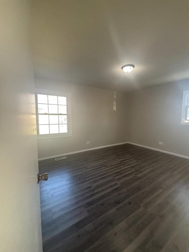 unfurnished room featuring baseboards, visible vents, and dark wood-type flooring