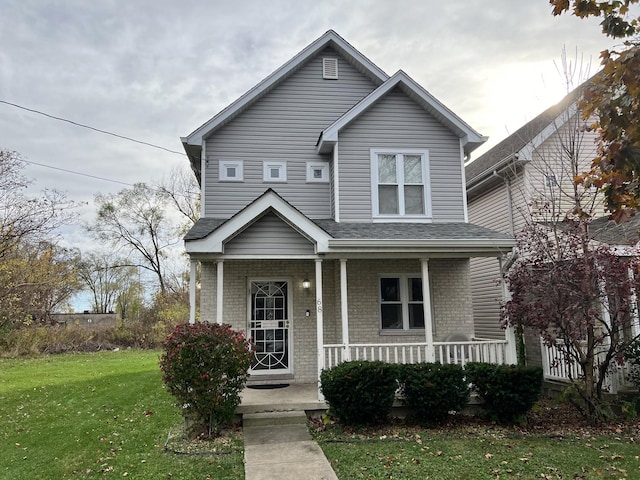 view of front of house with brick siding, covered porch, a shingled roof, and a front yard