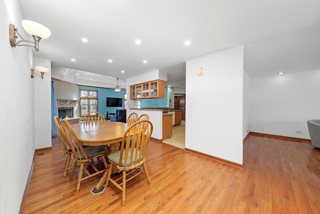 dining area with a stone fireplace, recessed lighting, and light wood-type flooring