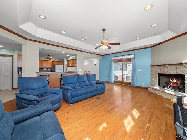 living room featuring light wood-style flooring, ceiling fan, crown molding, and a tray ceiling