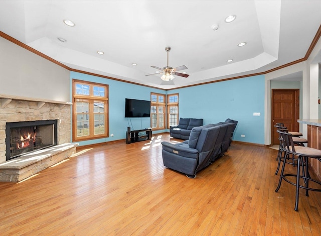 living room with crown molding, baseboards, light wood-type flooring, a tray ceiling, and a ceiling fan