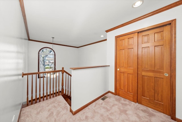 hallway with visible vents, crown molding, baseboards, an upstairs landing, and carpet flooring