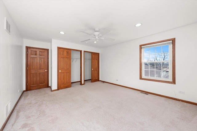 unfurnished bedroom with light carpet, visible vents, baseboards, and multiple closets