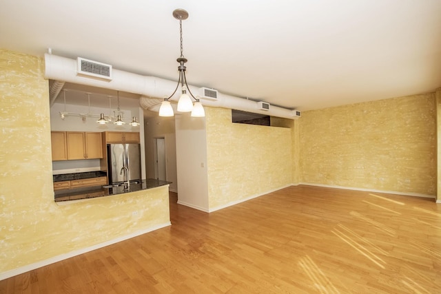 unfurnished living room with baseboards, light wood-style floors, visible vents, and a sink