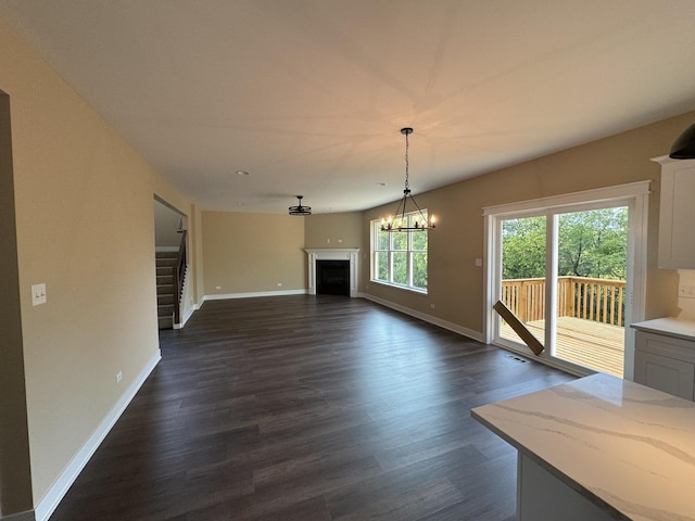 unfurnished living room featuring dark wood-type flooring, baseboards, stairs, a fireplace, and an inviting chandelier
