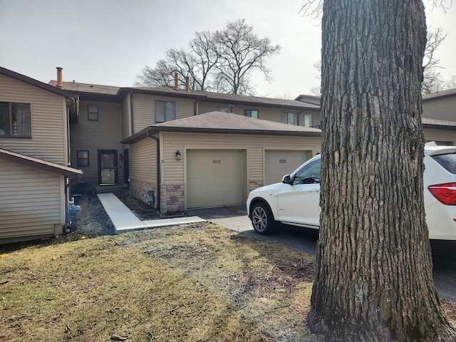 back of property with a garage, stone siding, and aphalt driveway