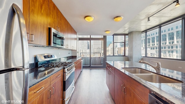 kitchen with a sink, stainless steel appliances, brown cabinets, and dark stone countertops